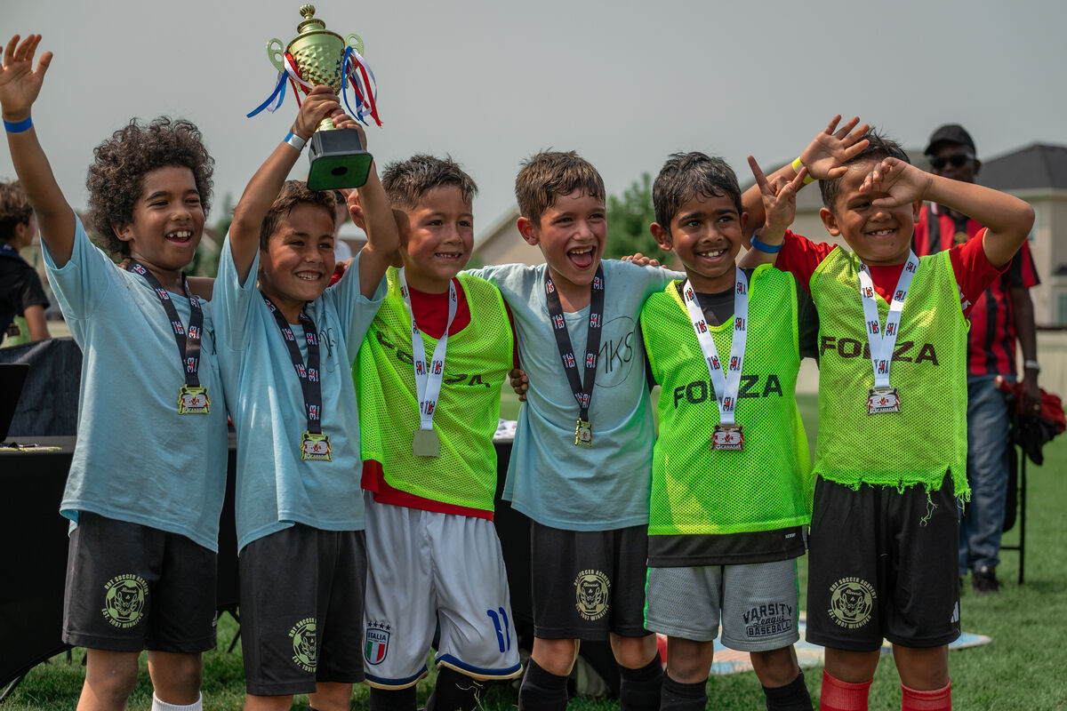 A crew of young players holding up a trophy and wearing medals after the RDT 3v3 AirPitch Tournament.