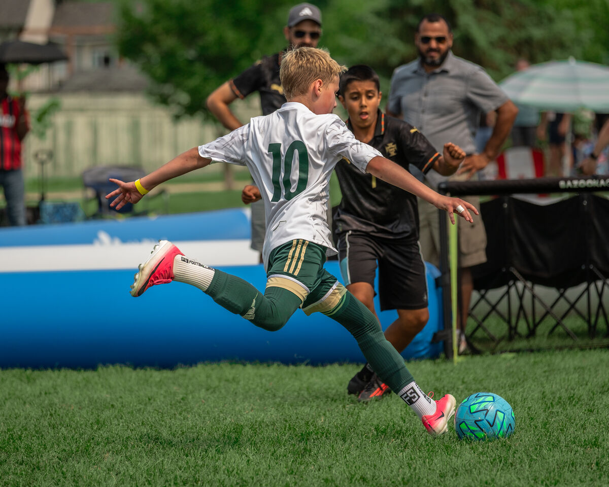 A player striking the ball at full stretch while an opponent closes in, inside the AirPitch.